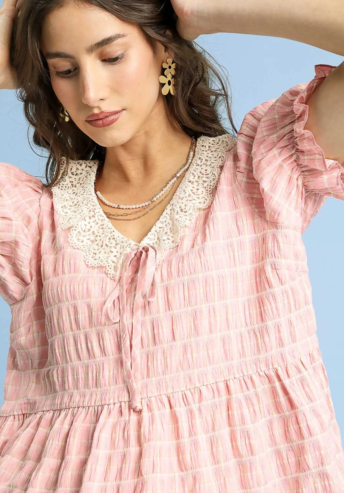 Woman wearing a pink blouse with lace details against a blue background