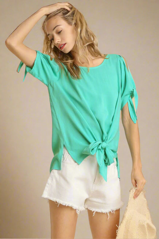 Woman wearing a turquoise top with tied sleeves and white shorts on a beige background