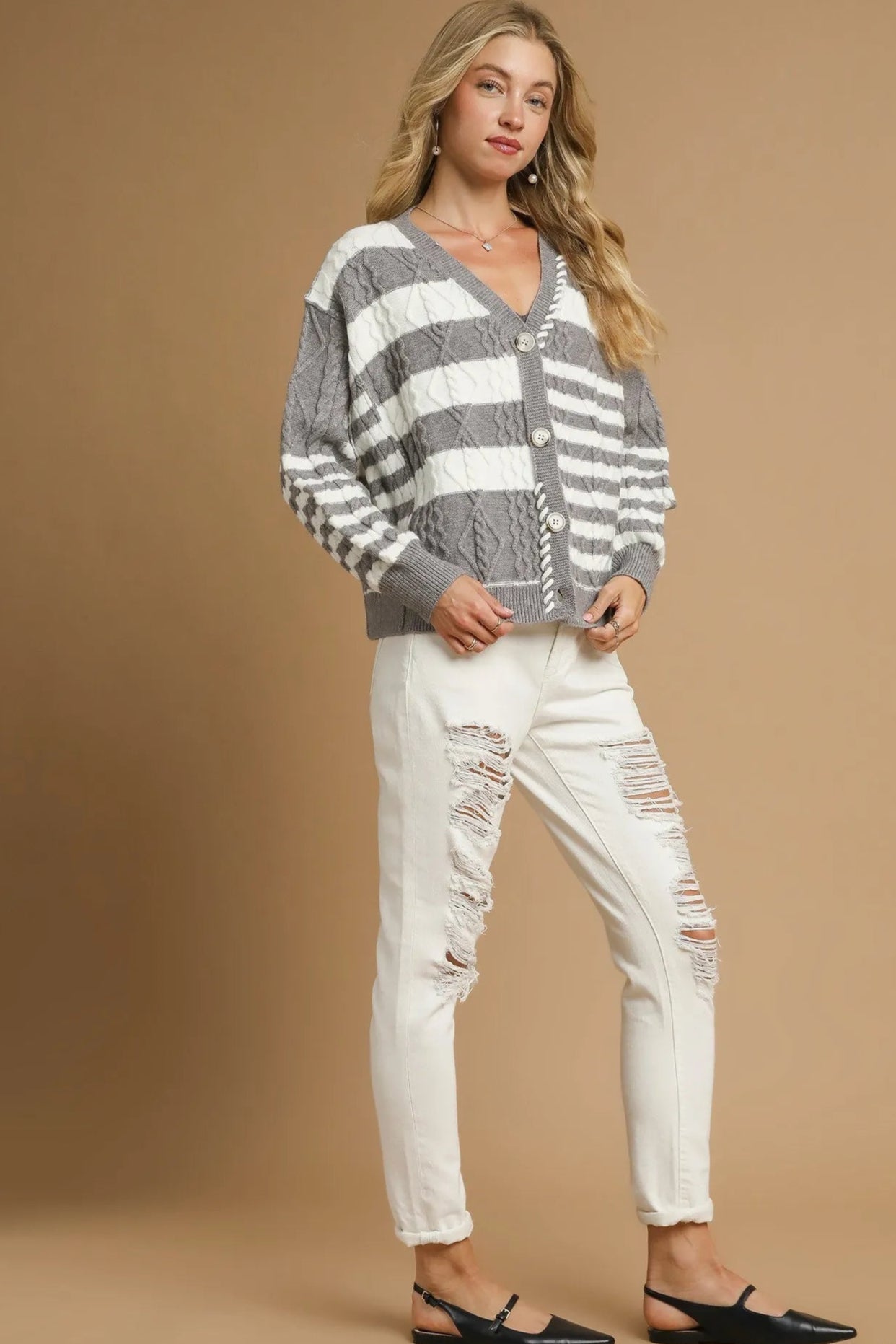 Woman wearing a gray and white striped sweater with white pants on a beige background