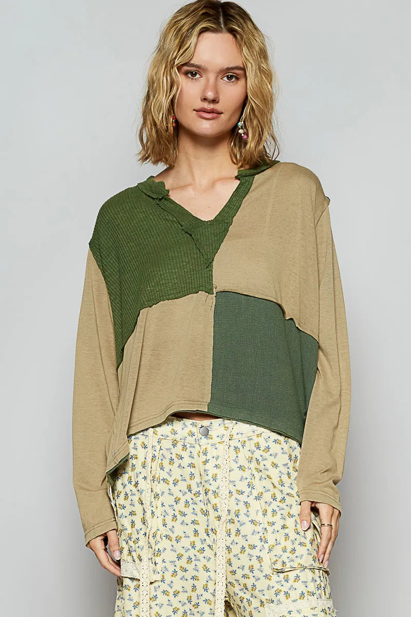 Woman wearing a green and beige patchwork top with floral pants on a plain background