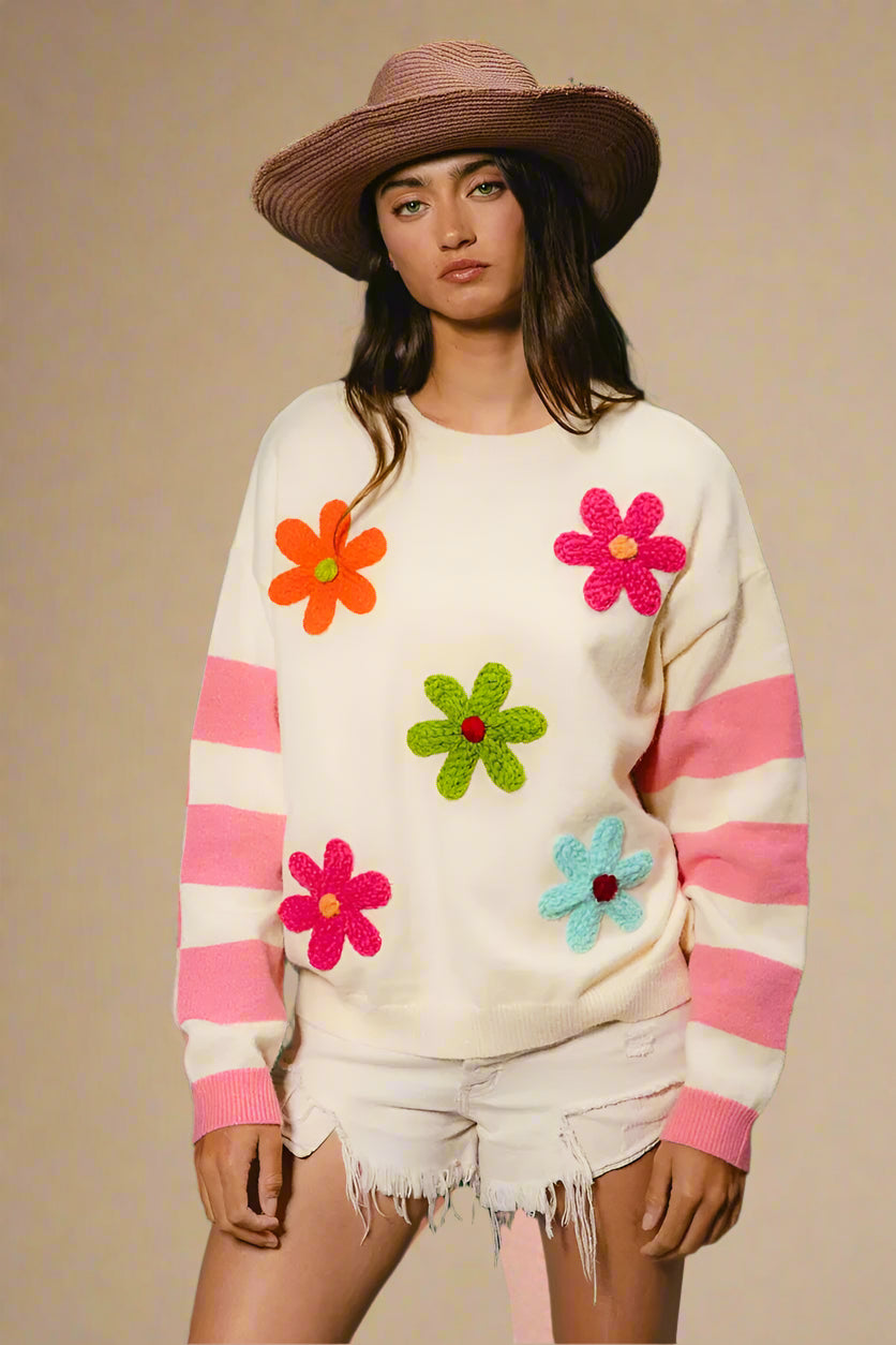 Woman wearing a cream sweater with colorful flower patterns against a green background