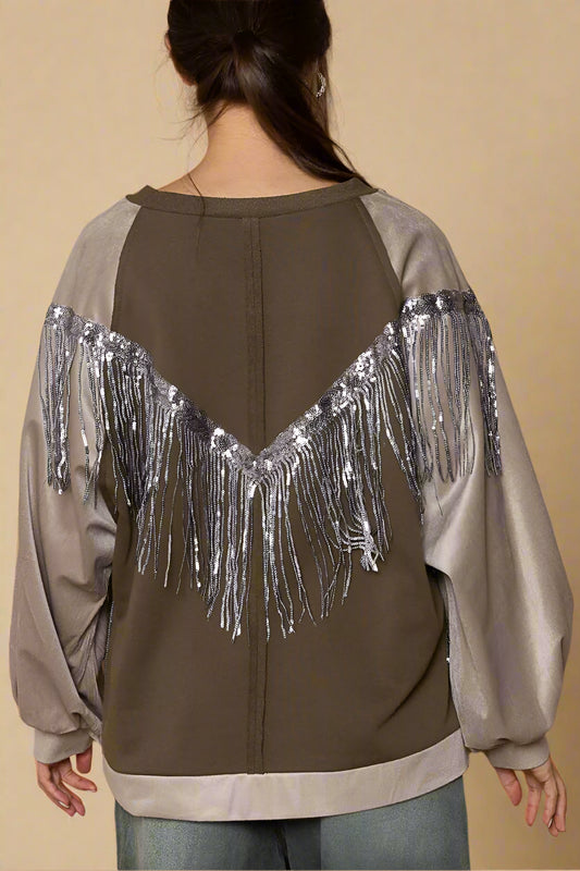 Person wearing a brown jacket with silver fringe details on a beige background