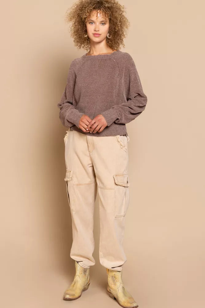 Woman wearing a brown sweater and beige cargo pants against a beige background