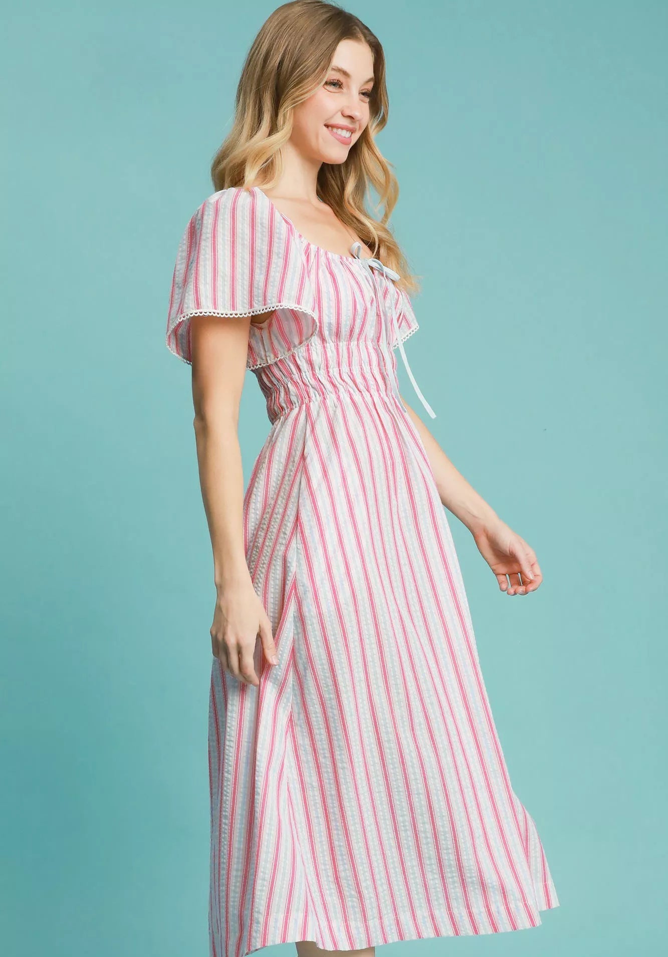 Woman wearing a pink and blue striped dress on a teal background