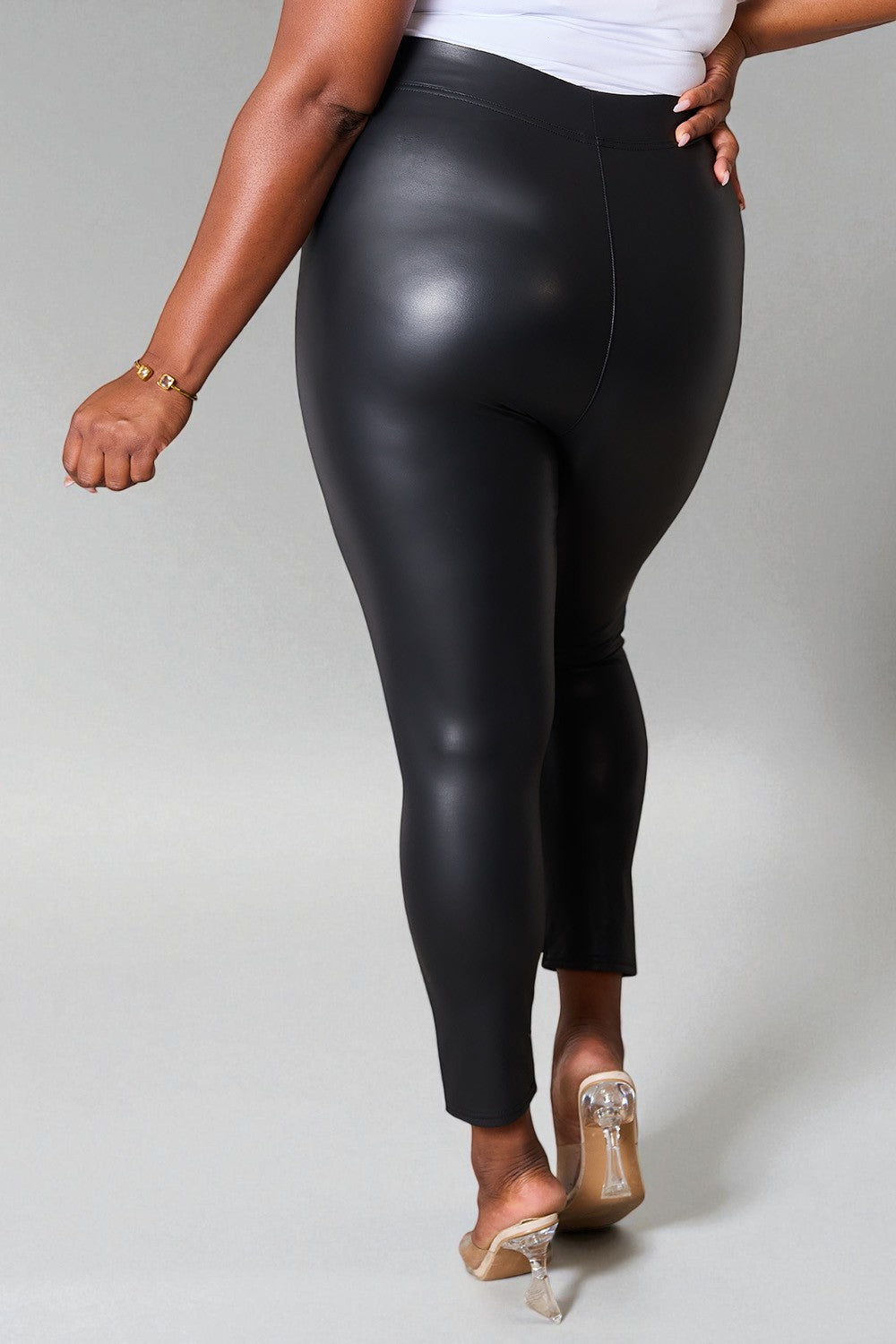 Person wearing black shiny leggings on a plain background