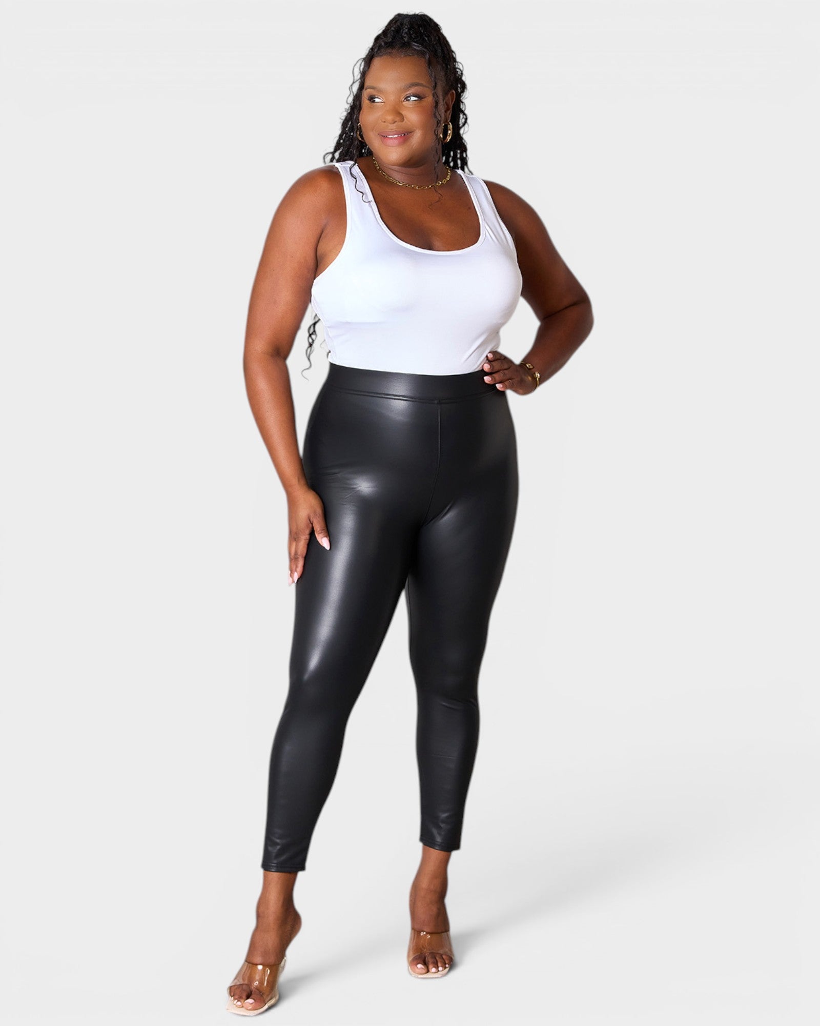 Woman wearing black leather leggings and a white tank top on a white background