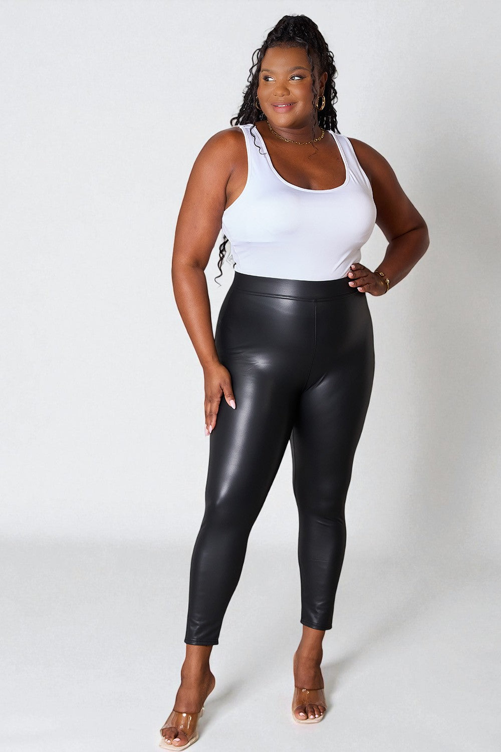 Woman wearing a white tank top and black leather leggings on a white background