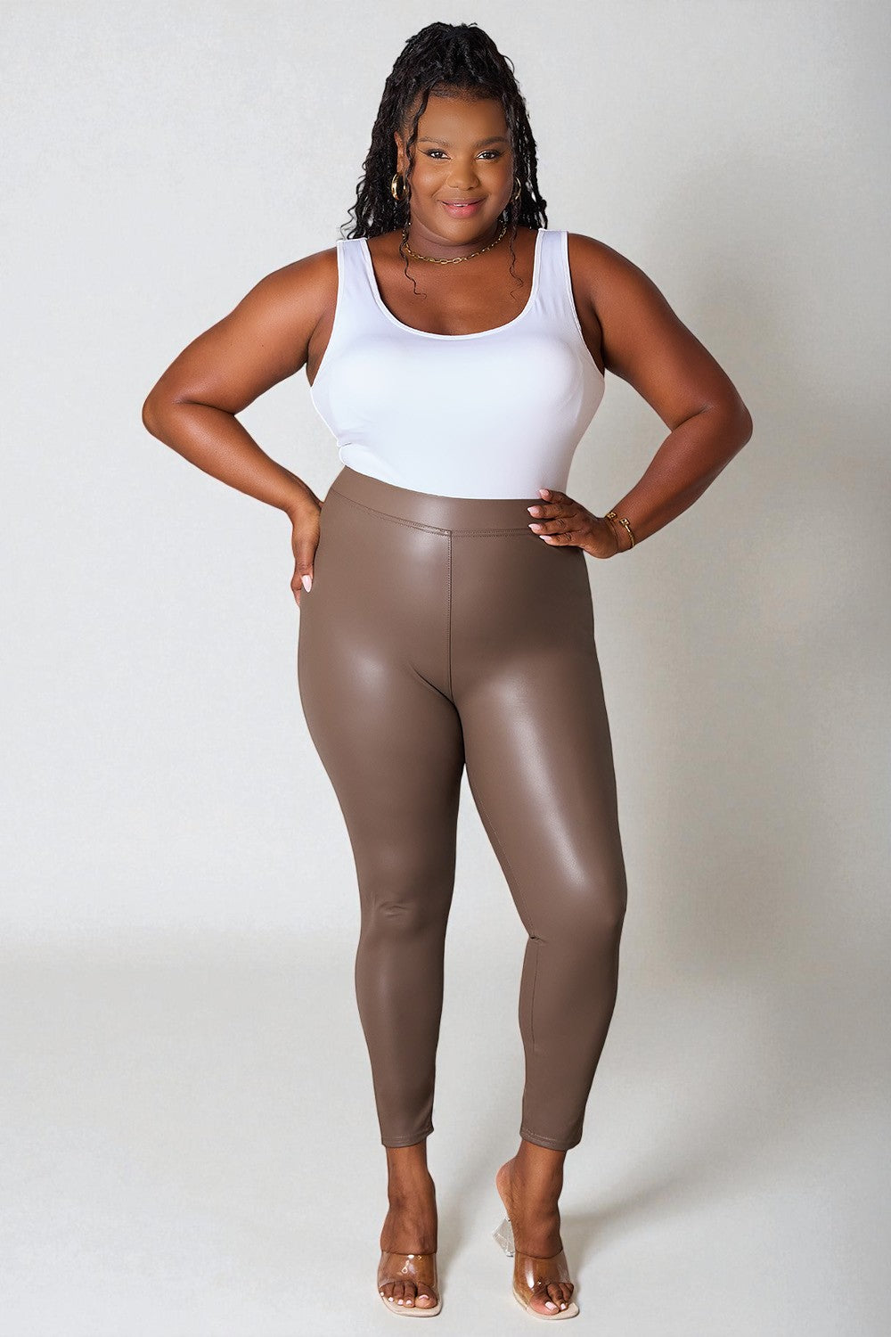 Person wearing a white tank top and brown leather leggings on a plain background