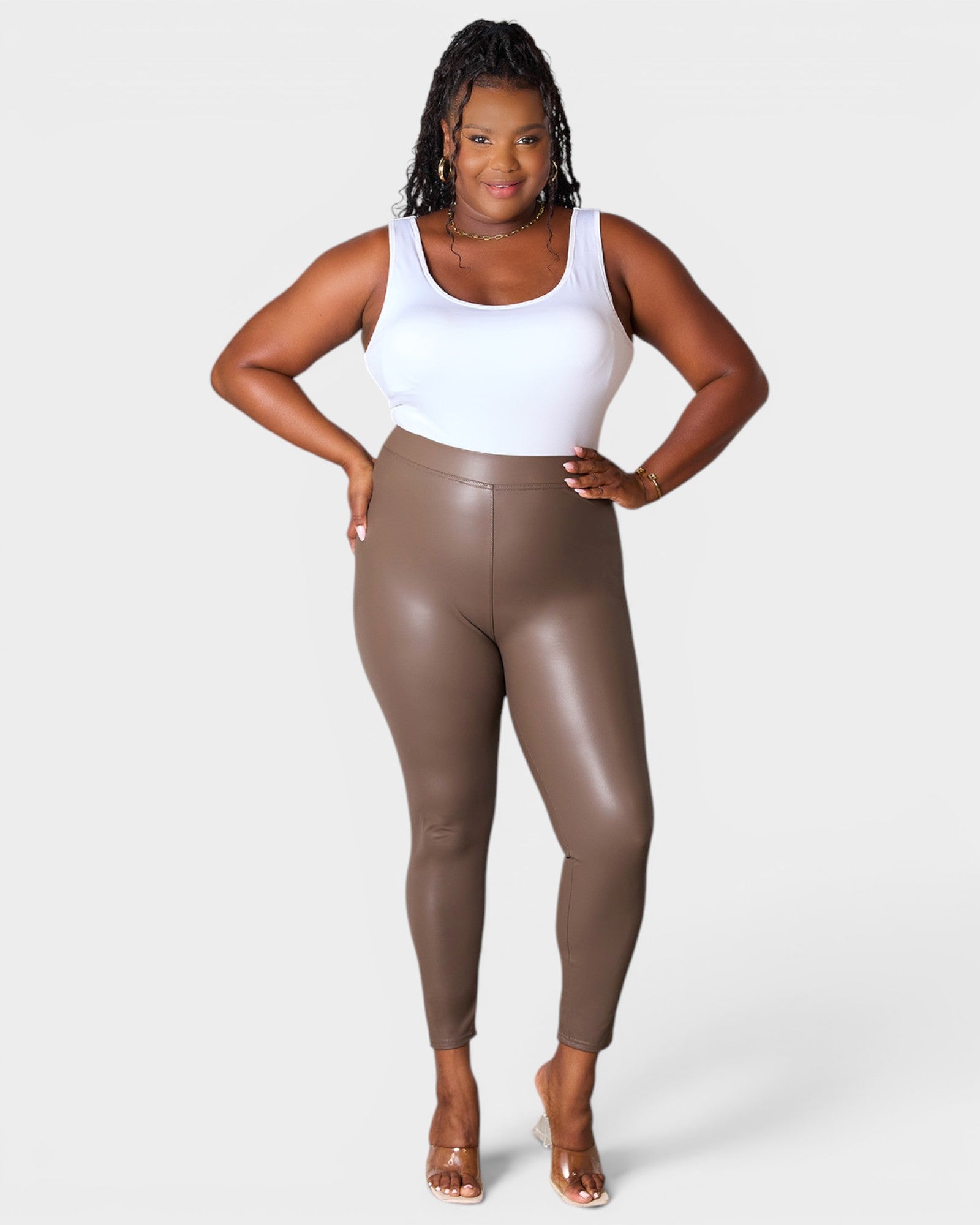 Woman wearing brown leather leggings and a white tank top on a white background
