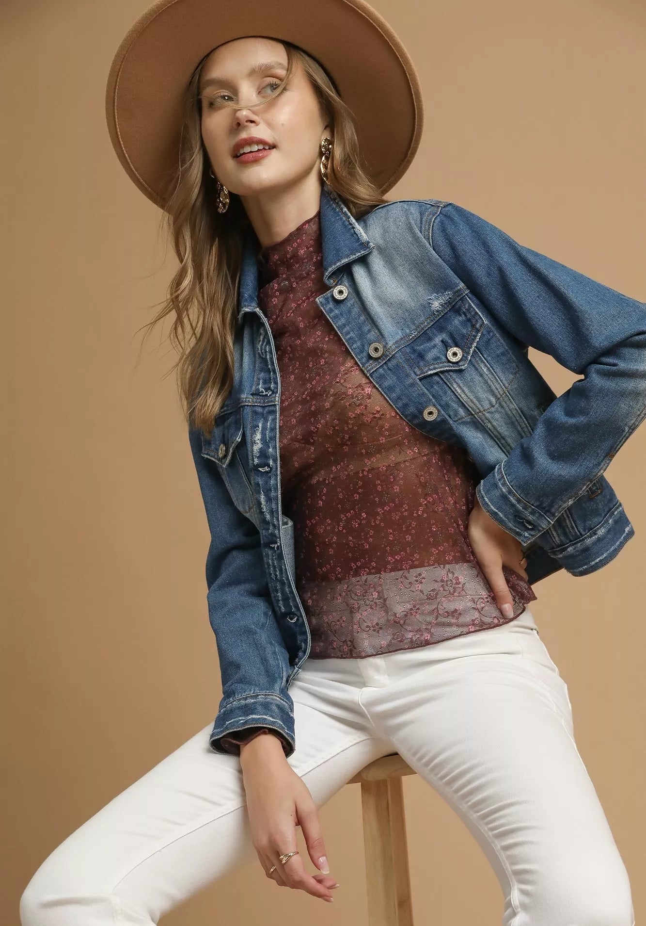 Woman wearing a denim jacket, burgundy sweater, and white pants on a beige background
