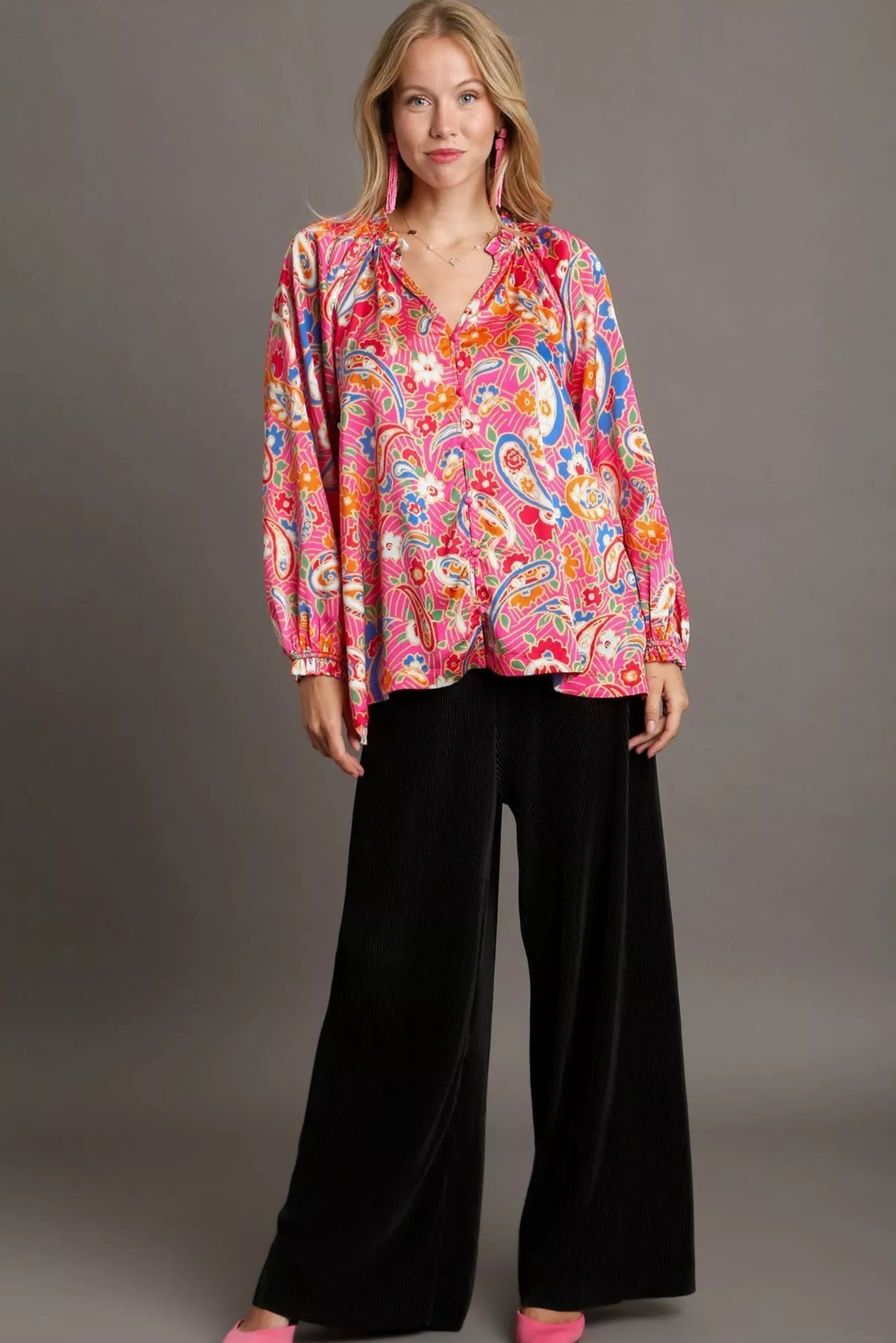 Woman wearing a colorful patterned blouse and black pants on a gray background