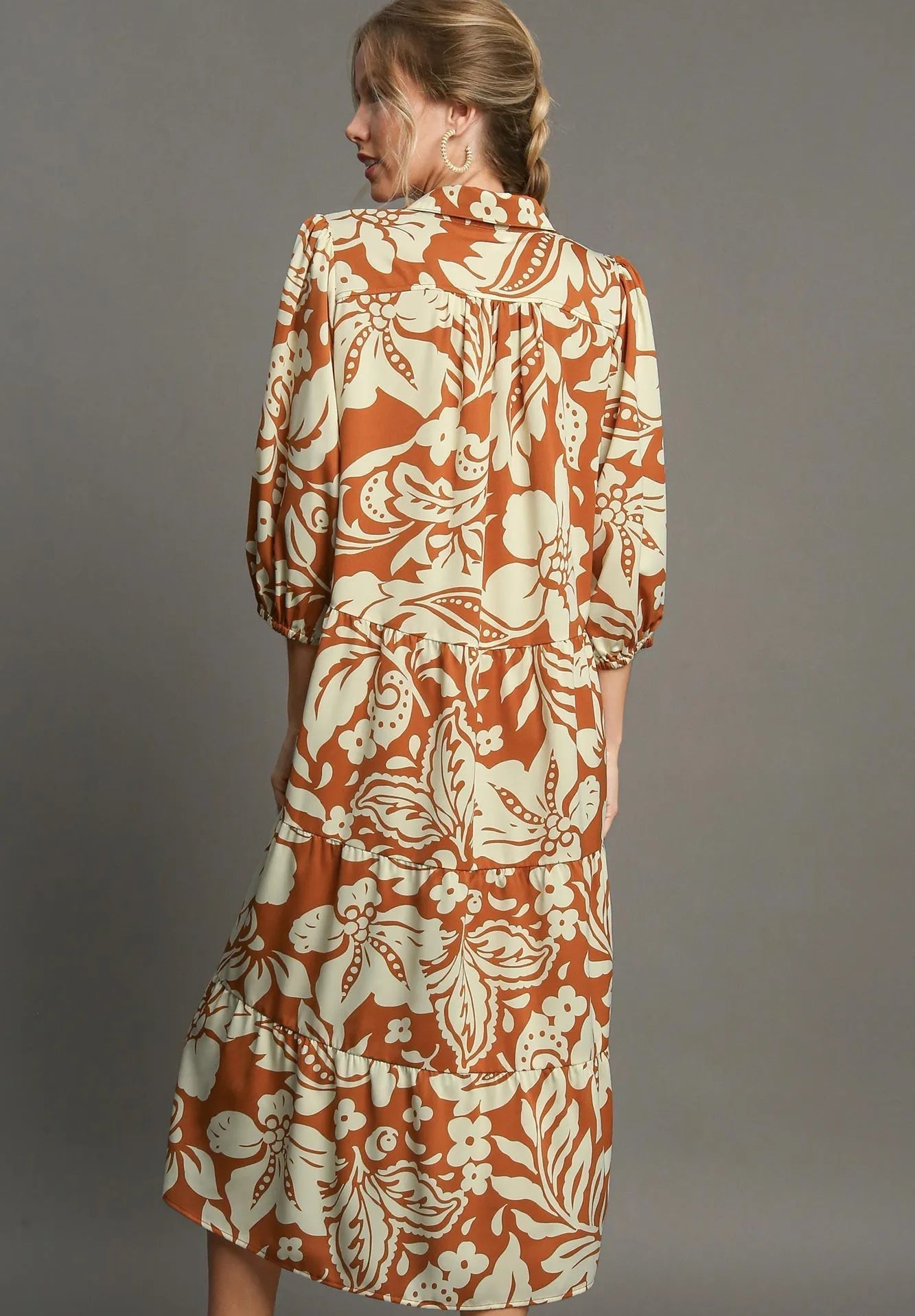 Woman wearing a rust and beige floral dress against a gray background