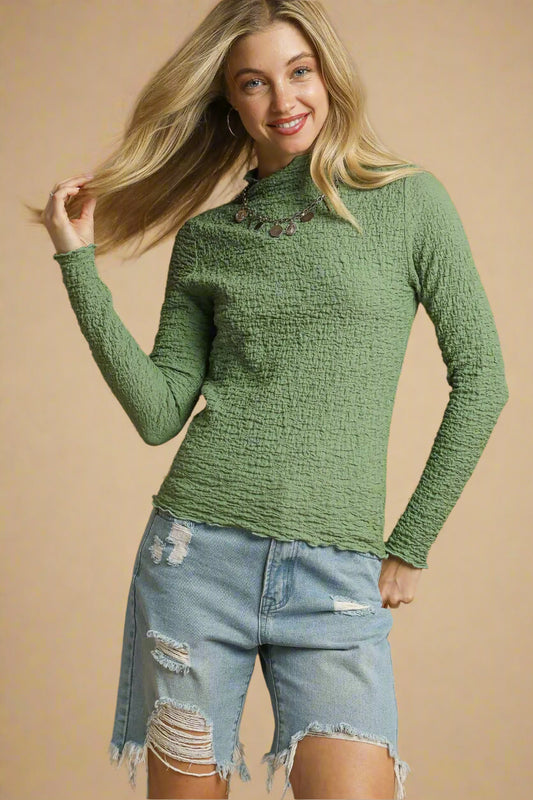 Woman wearing a green textured sweater and denim shorts on a beige background