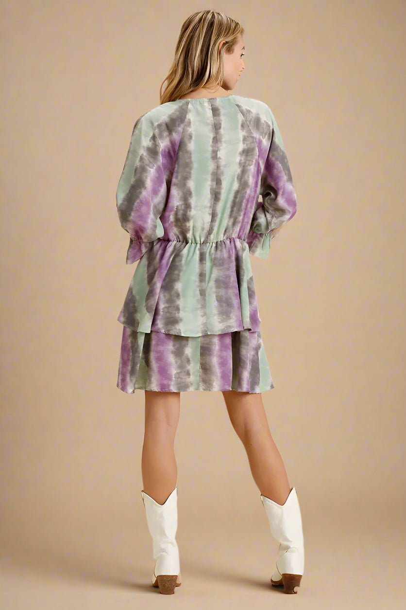 Woman wearing a green and purple tie-dye dress with white boots on a beige background