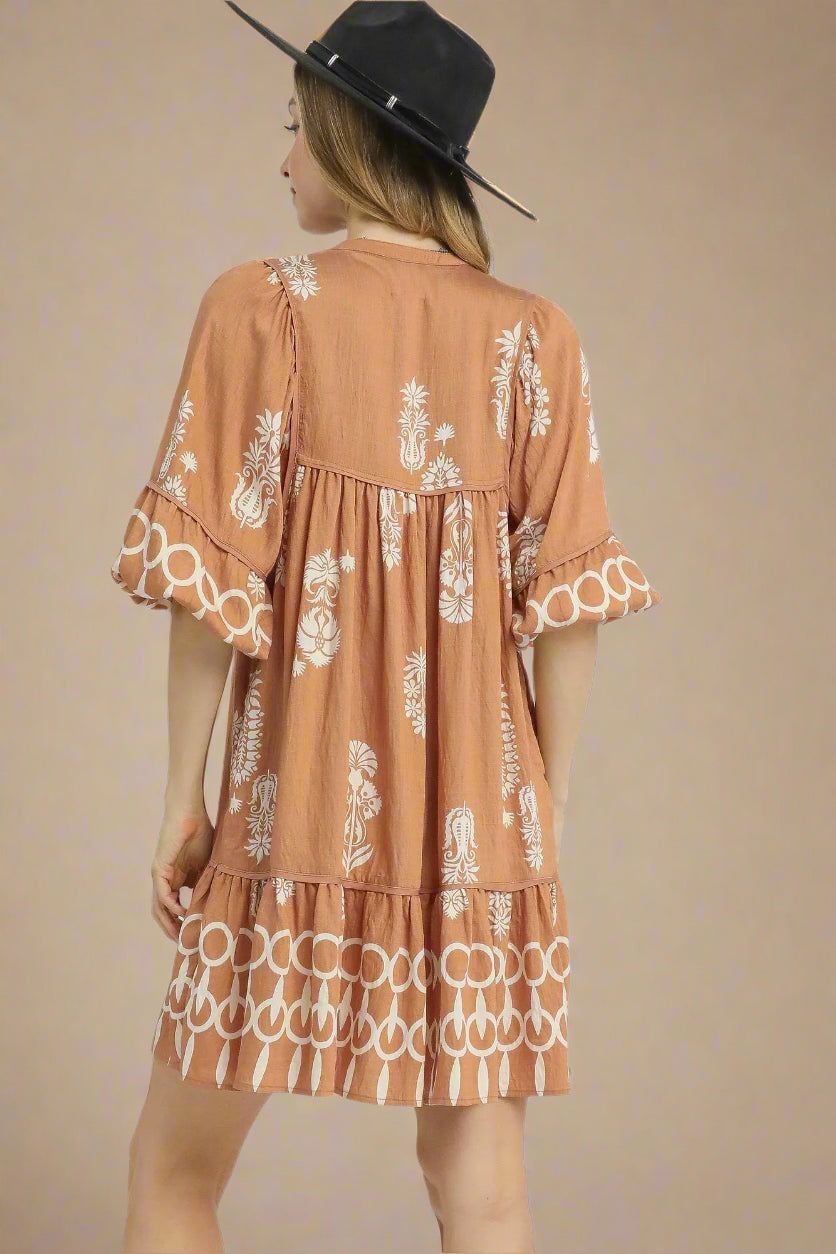 Woman wearing a brown dress with white patterns and a black hat on a light gray background