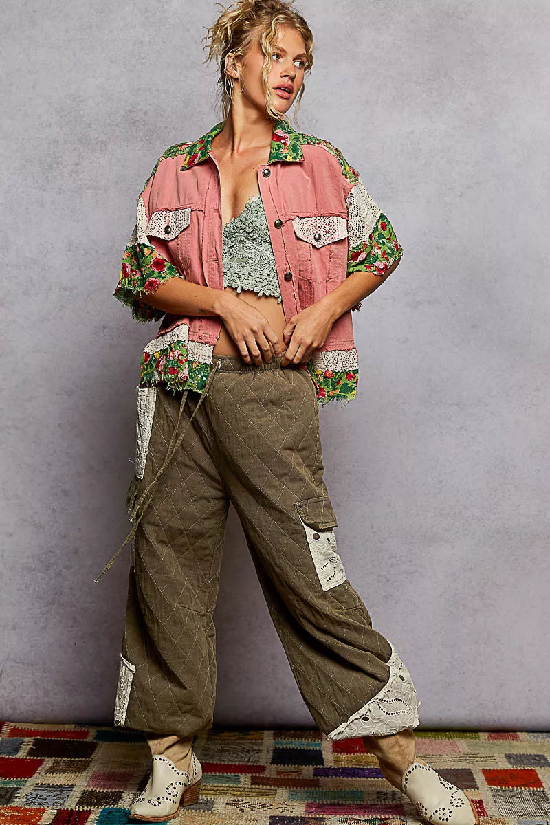 Person wearing a floral jacket over a patterned top with green pants against a gray background