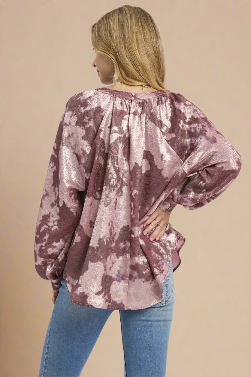 Woman wearing a tie-dye blouse in merlot color with blue jeans on a beige background