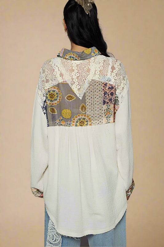Person wearing a white blouse with floral patchwork design on a plain background