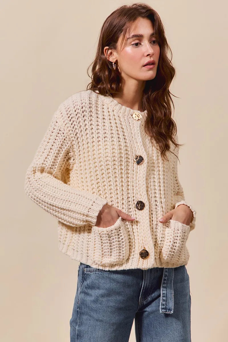 Woman wearing a beige knitted cardigan with button details on a beige background