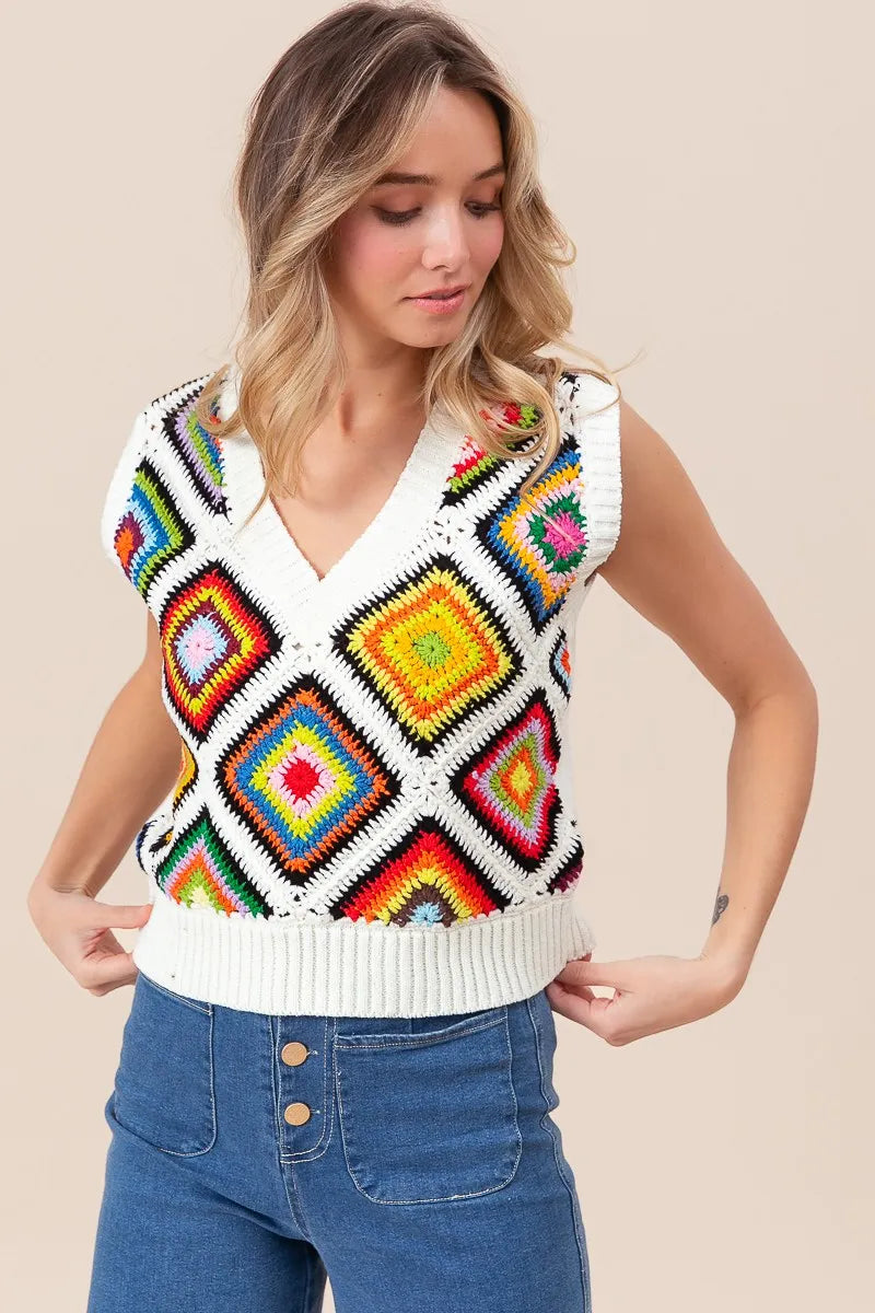 Woman wearing a colorful patterned sleeveless sweater over a white shirt with blue jeans on a beige background