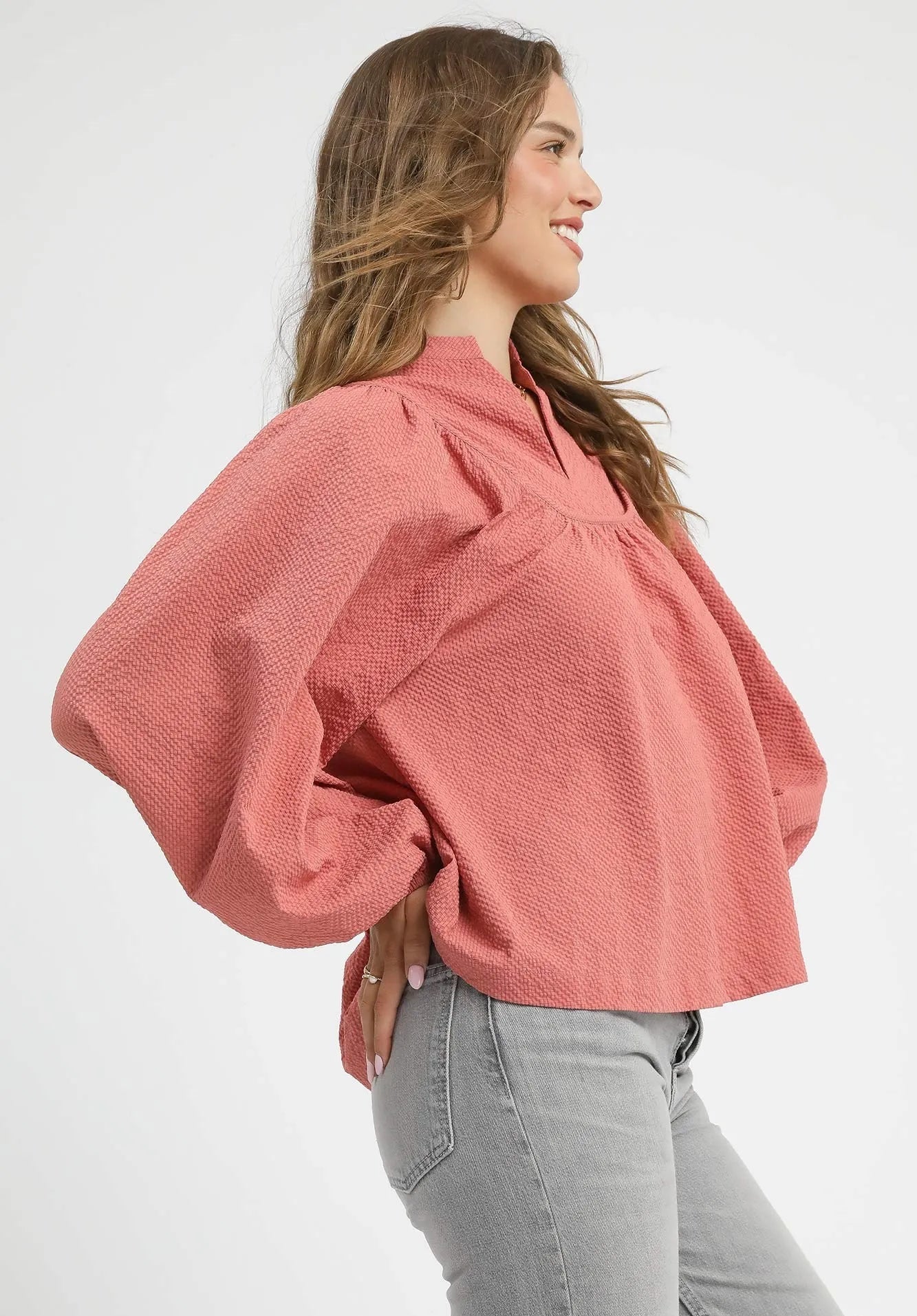 Woman wearing a dusty rose blouse with balloon sleeves on a white background