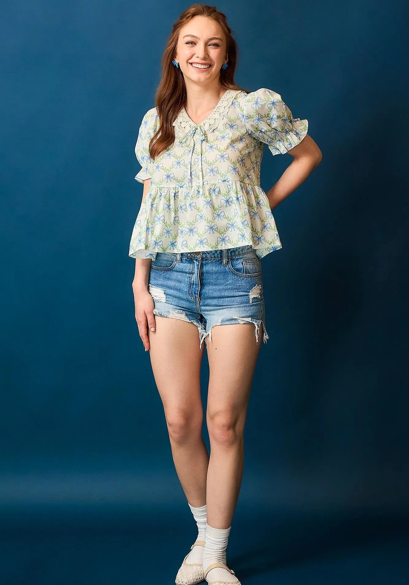Woman wearing a floral blouse and denim shorts against a blue background
