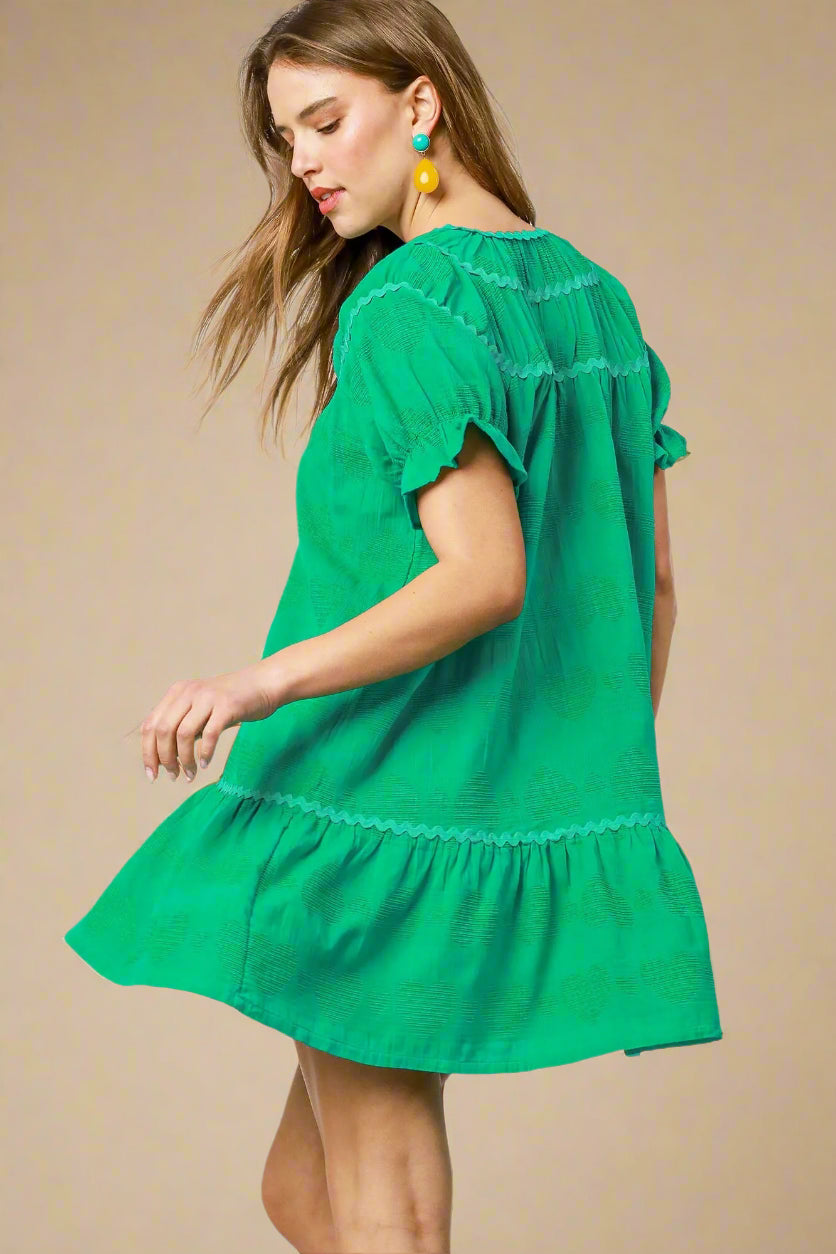 Woman wearing a green dress with ruffled sleeves and hem on a white background