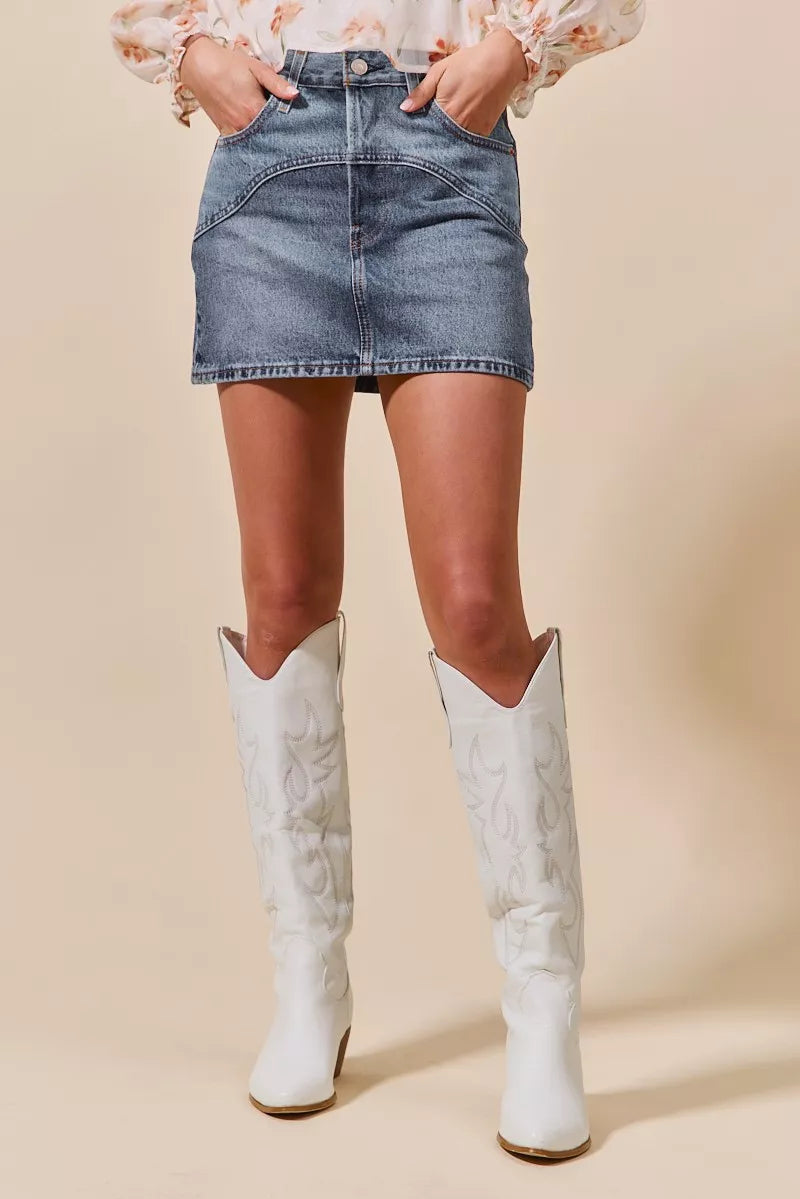 Person wearing a denim skirt and white cowboy boots on a beige background