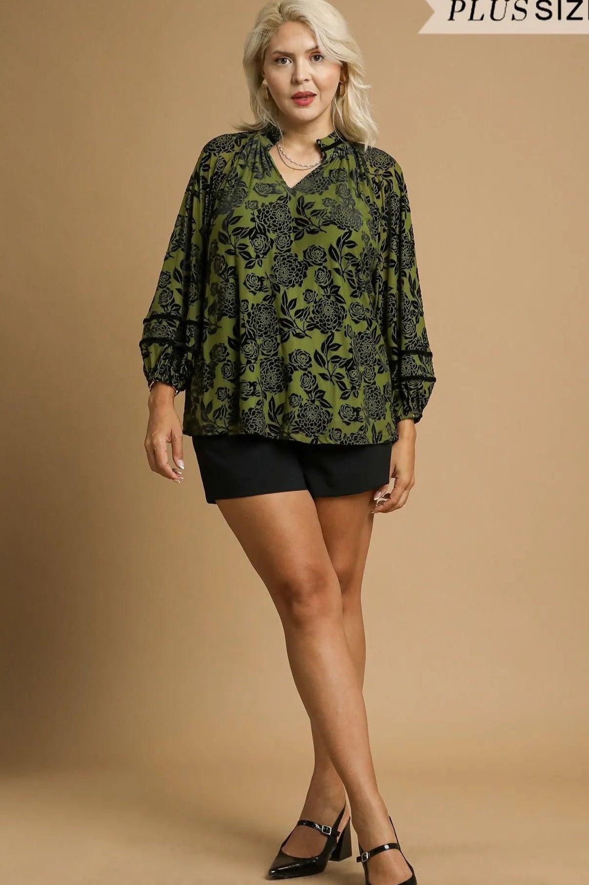 Woman wearing a green patterned blouse and black shorts on a beige background