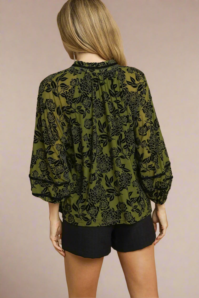 Person wearing a green floral blouse with black patterns on a beige background