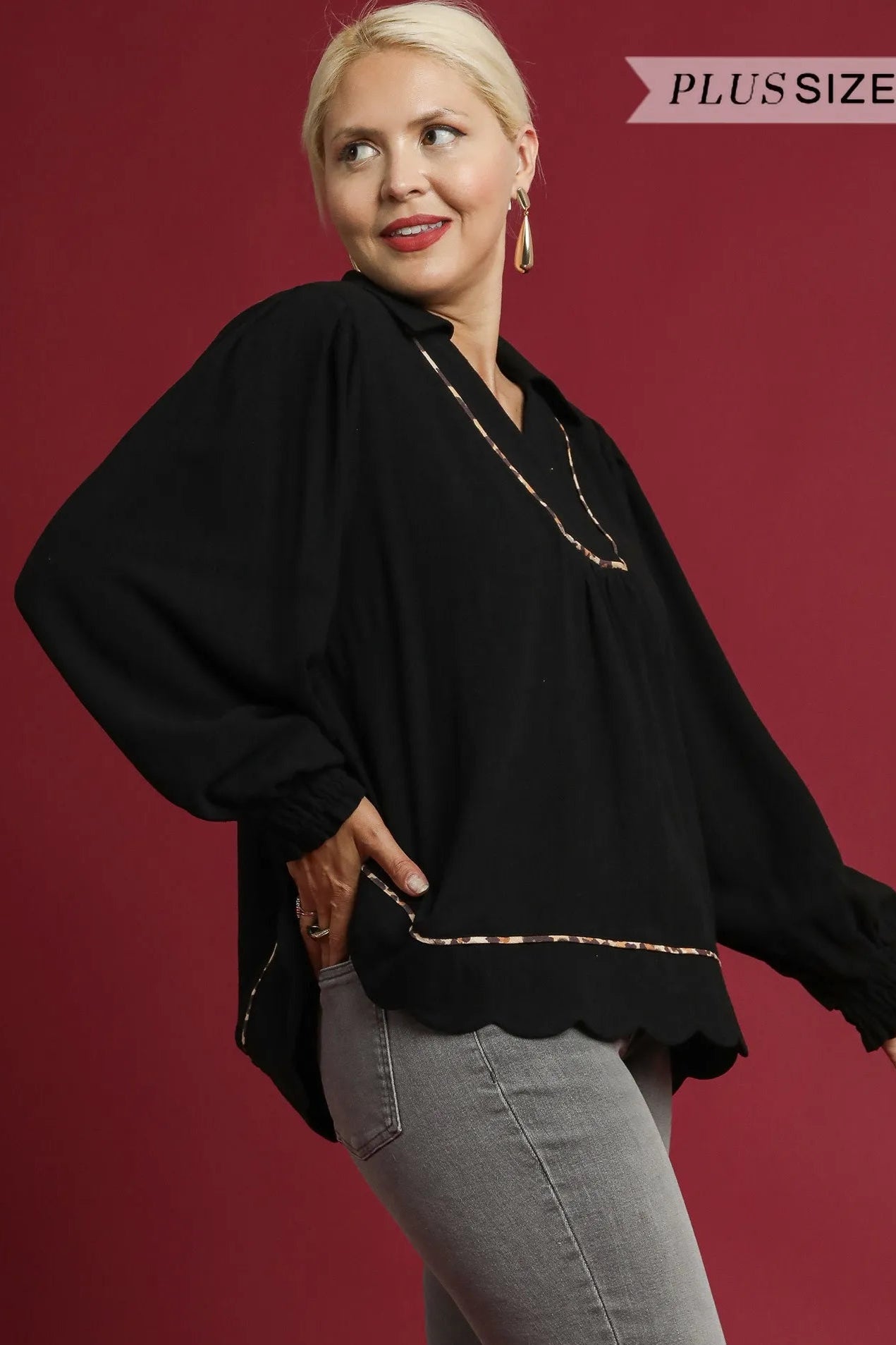 Woman wearing a black top with gold trim against a red background