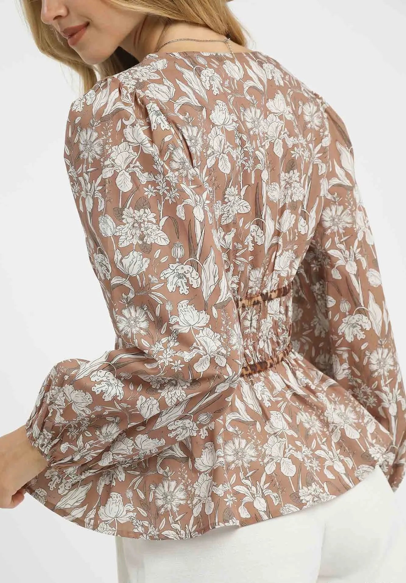 Light brown floral blouse worn by a person on a white background