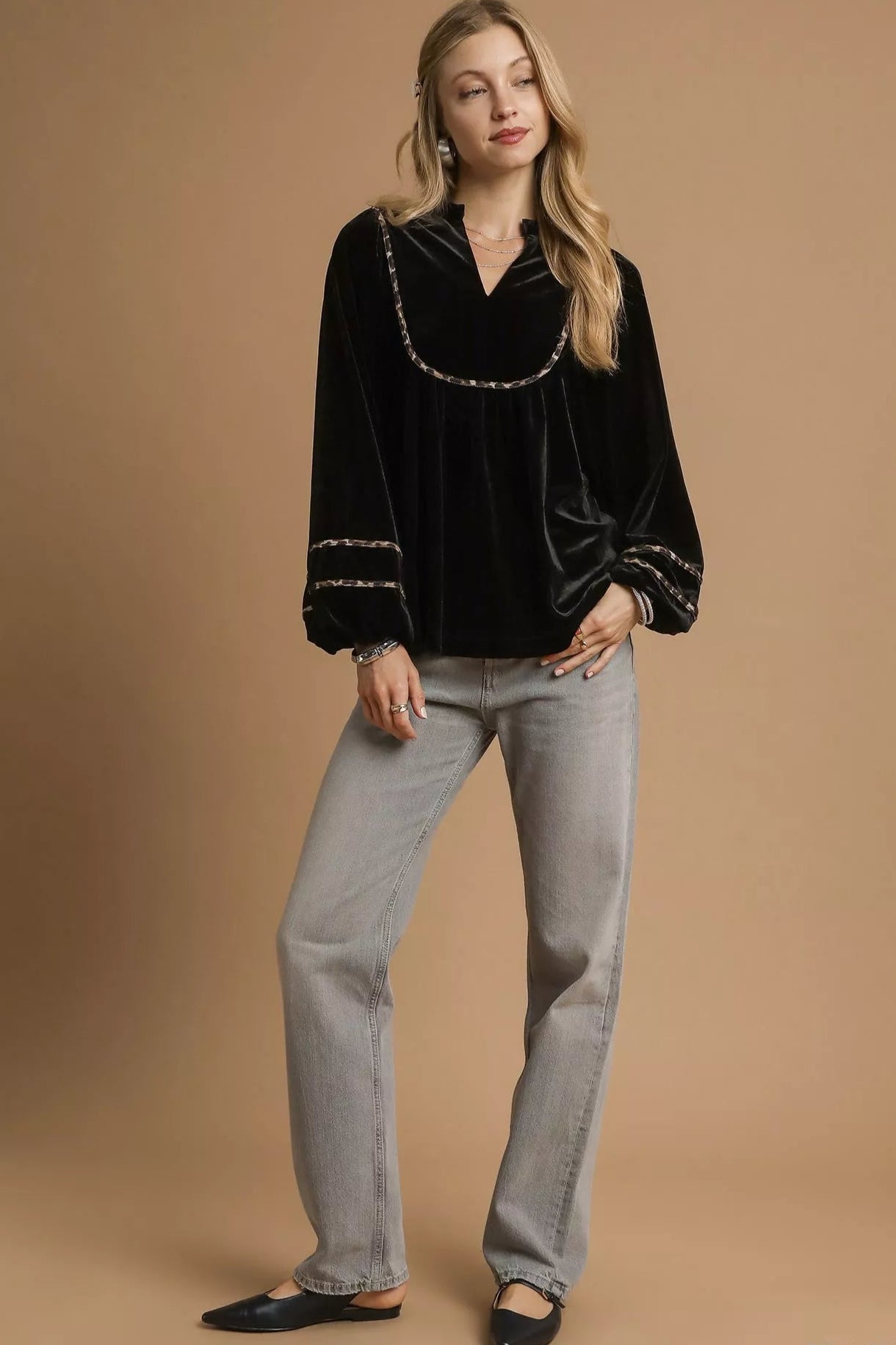 Woman wearing a black velvet top with silver trim and gray pants on a beige background