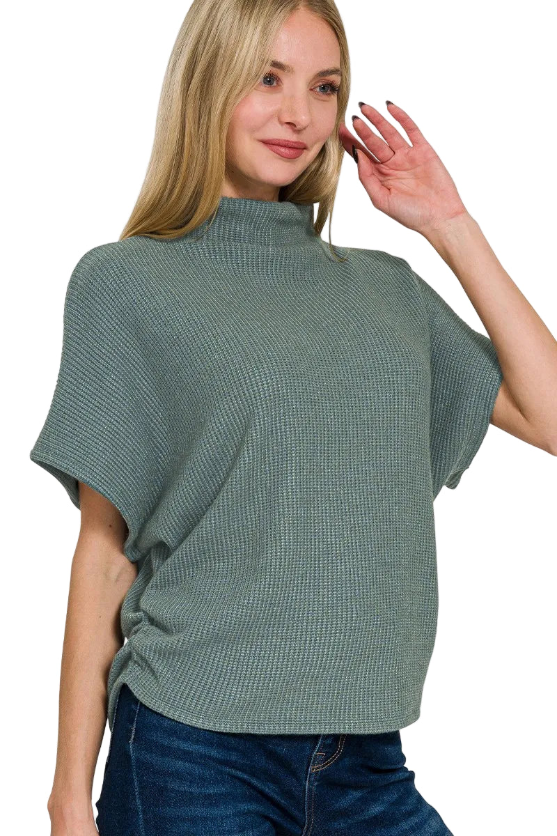 Woman wearing a green knit top with short sleeves on a white background