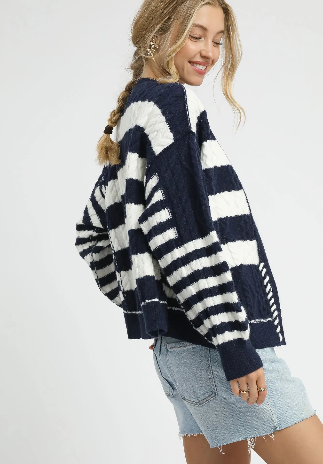 Woman wearing a navy and white striped sweater with denim shorts on a white background