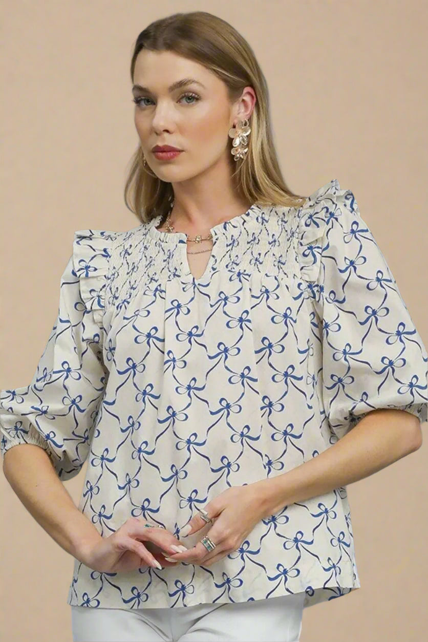 Woman wearing a white blouse with blue patterns against a beige background