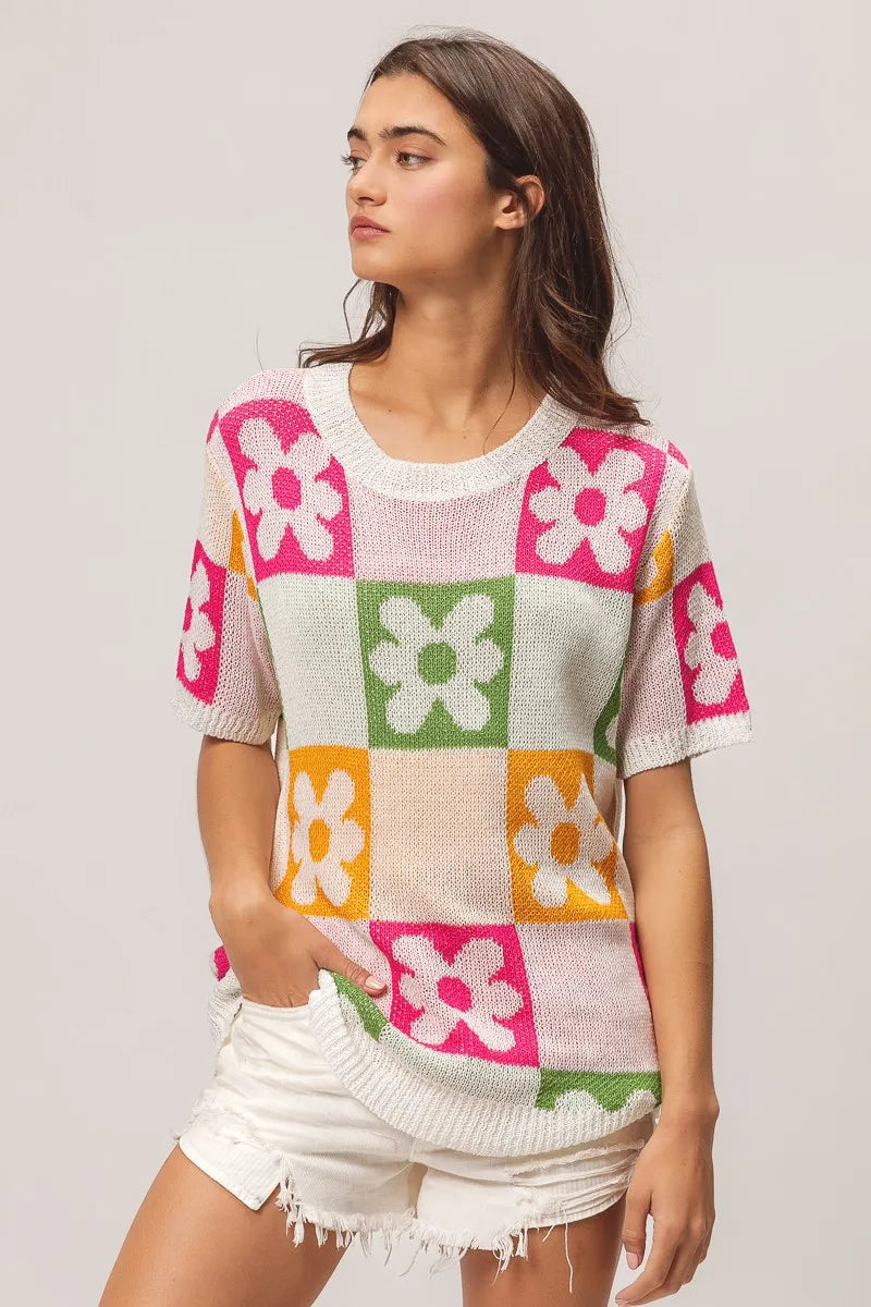 Woman wearing a colorful checkered sweater with flower patterns on a plain background