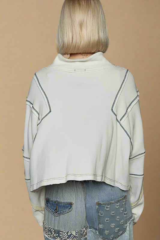 Person wearing a light-colored sweater with geometric patterns over a denim outfit on a beige background