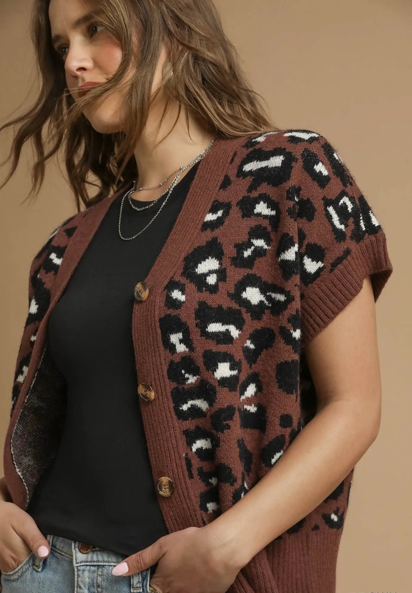 Woman wearing a brown leopard print cardigan against a beige background
