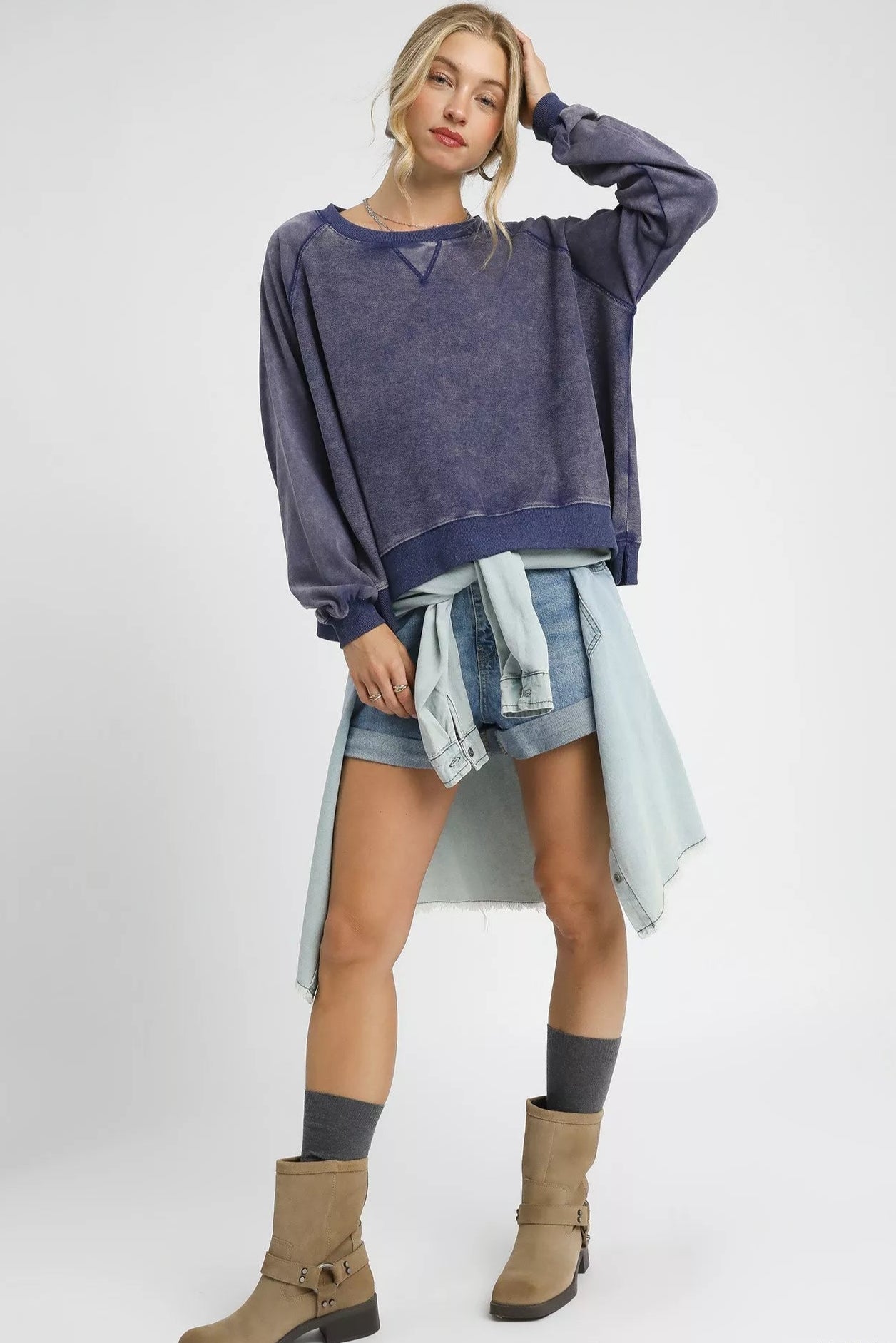 Woman wearing a navy sweater, denim shorts, and brown boots on a white background