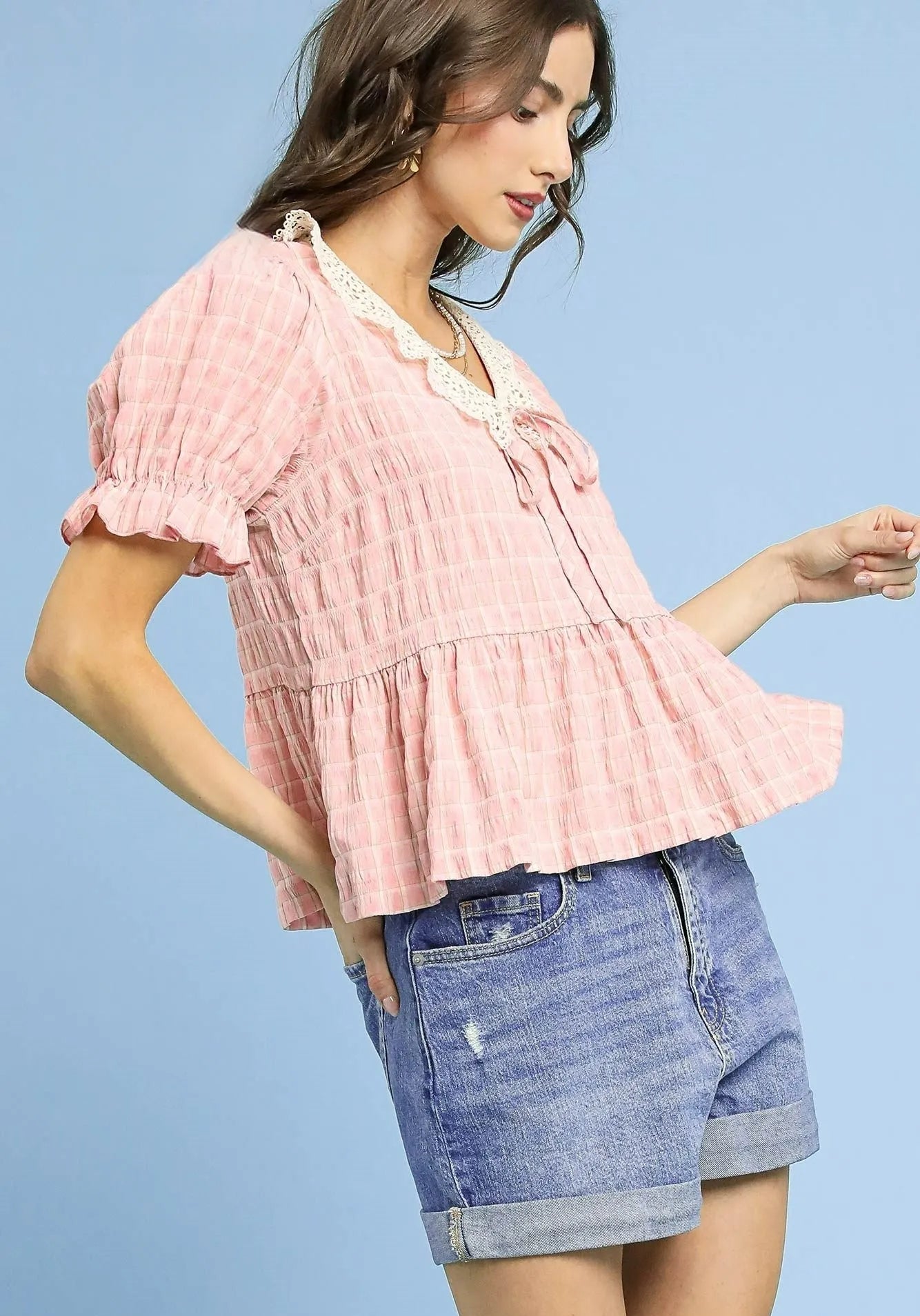 Woman wearing a pink ruffled blouse and denim shorts against a light blue background