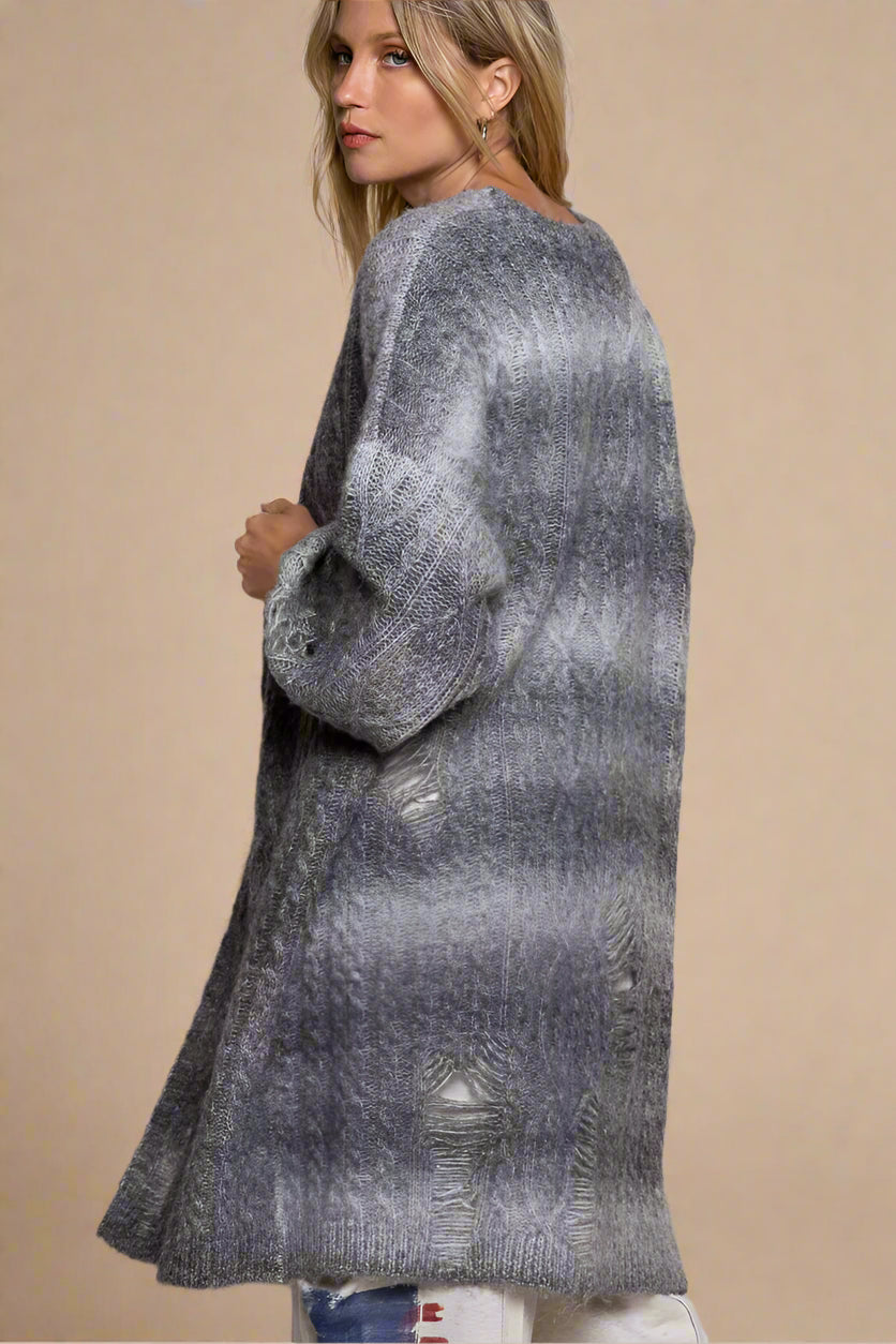 Woman wearing a long, patterned gray sweater against a plain background