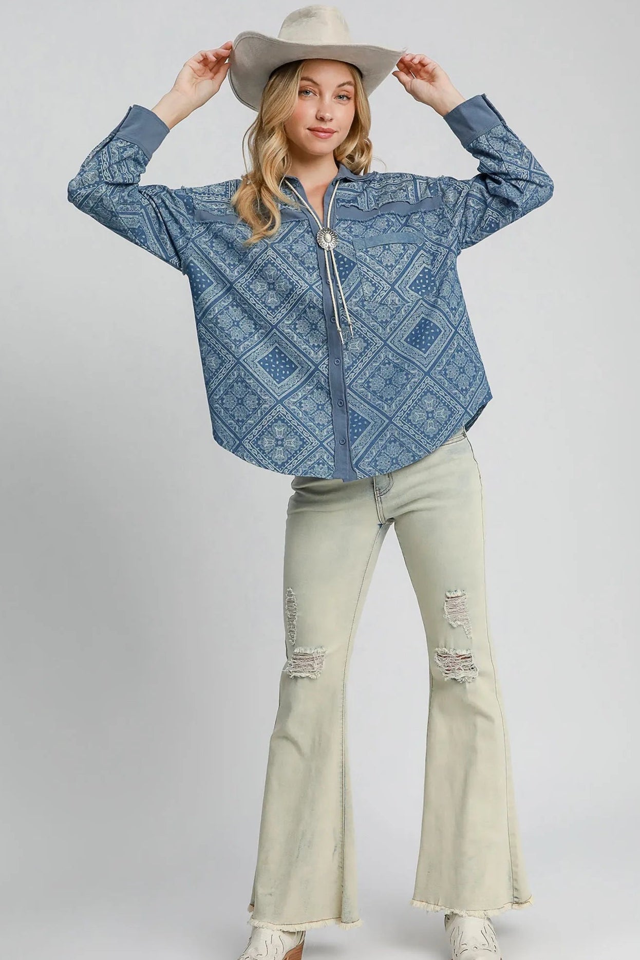 Woman wearing a light denim patterned shirt and light green pants on a white background