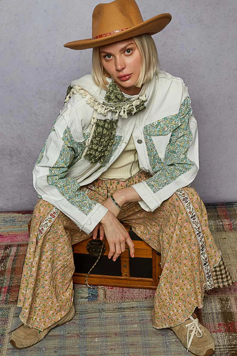 Person wearing a stylish outfit with a hat, scarf, and patterned pants sitting on a wooden box.