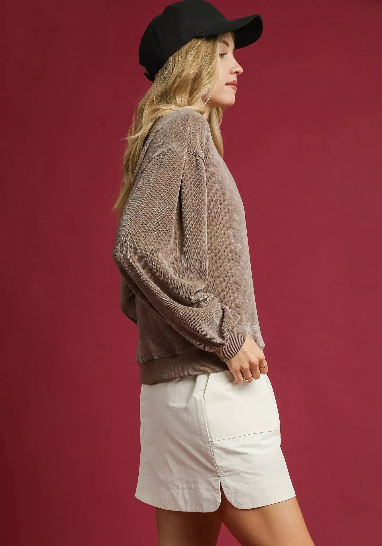 Woman wearing a brown sweater and white shorts against a red background