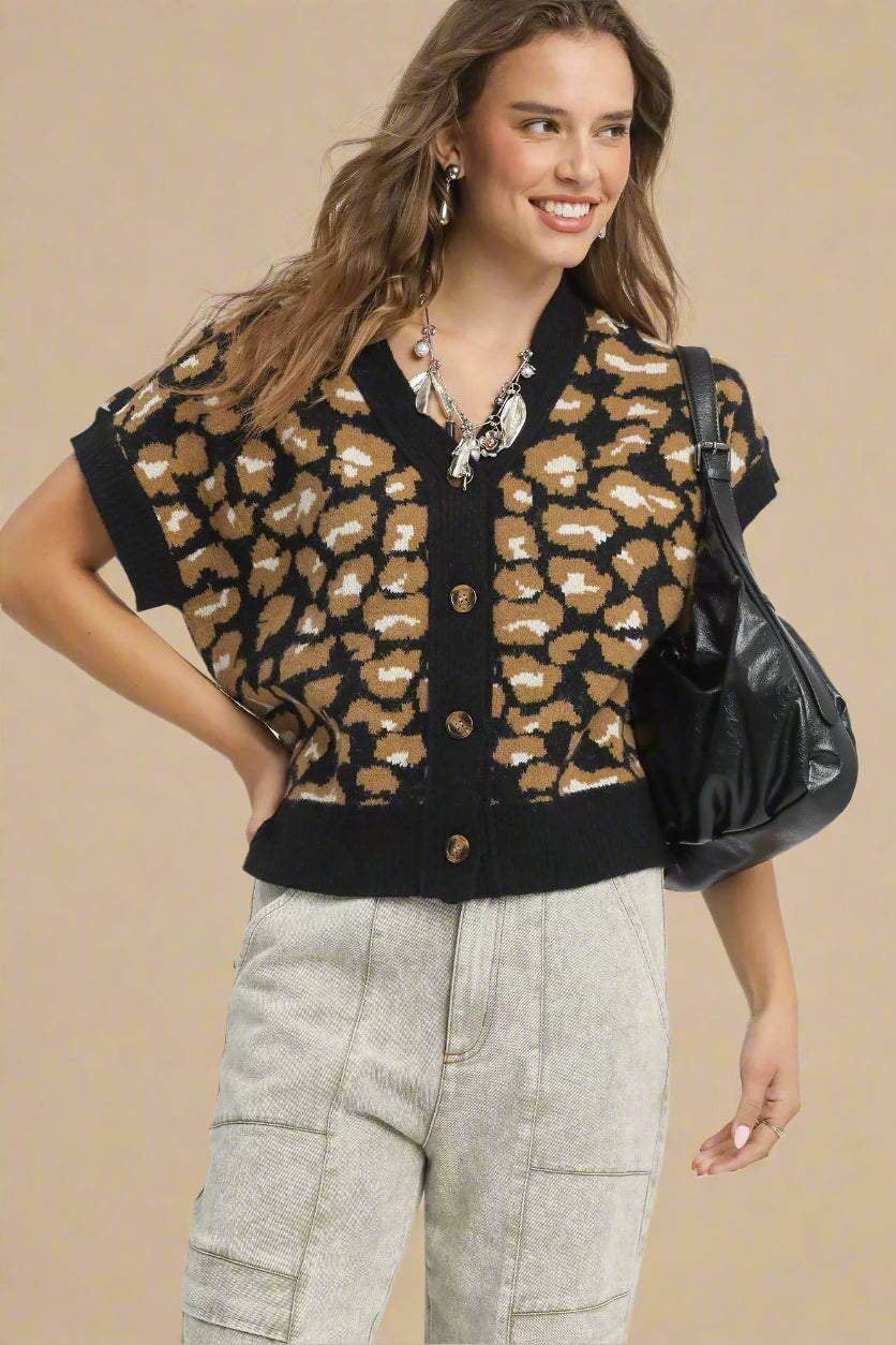 Woman wearing a black and brown leopard print cardigan with gray pants on a beige background