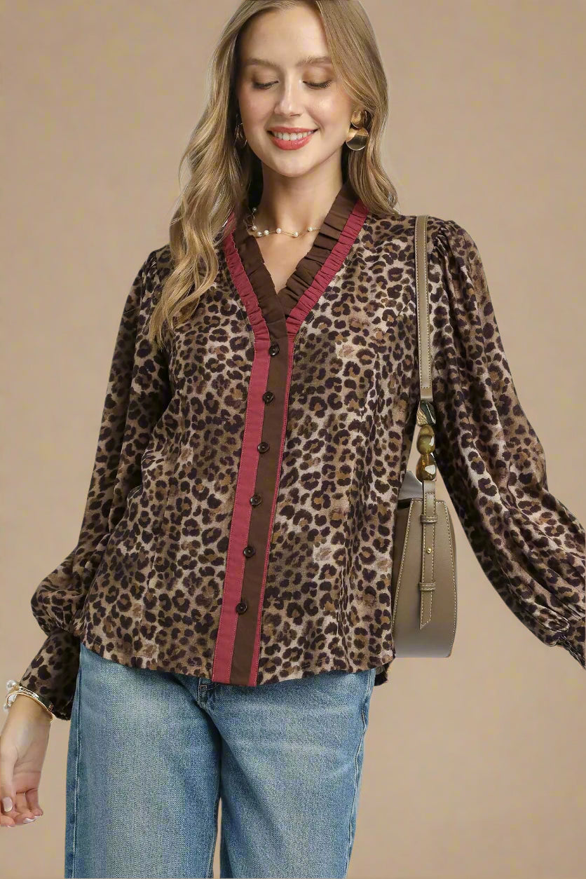 Woman wearing a leopard print blouse with red trim and blue jeans, holding a brown handbag on a beige background.