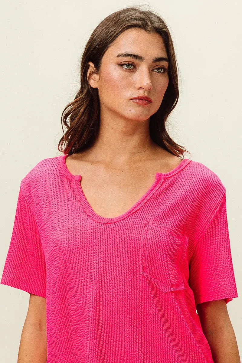 Woman wearing a bright pink textured top against a plain background
