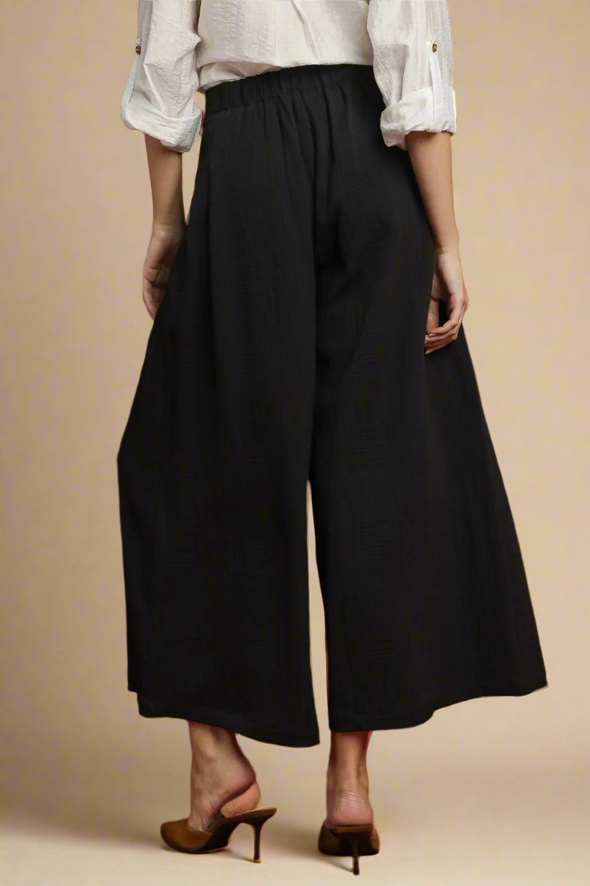 Person wearing black wide-leg pants on a beige background