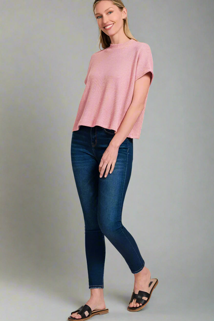 Woman wearing a light pink top and blue jeans on a white background